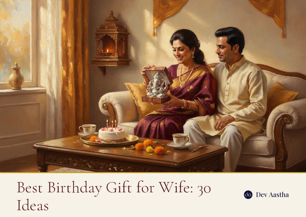 An Indian wife opening a birthday gift box with a silver-plated idol inside, beside a cake and marigolds in a warmly lit living room