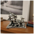Silver Ganesha idol lying with an open book and a bowl of sweets on a wooden surface