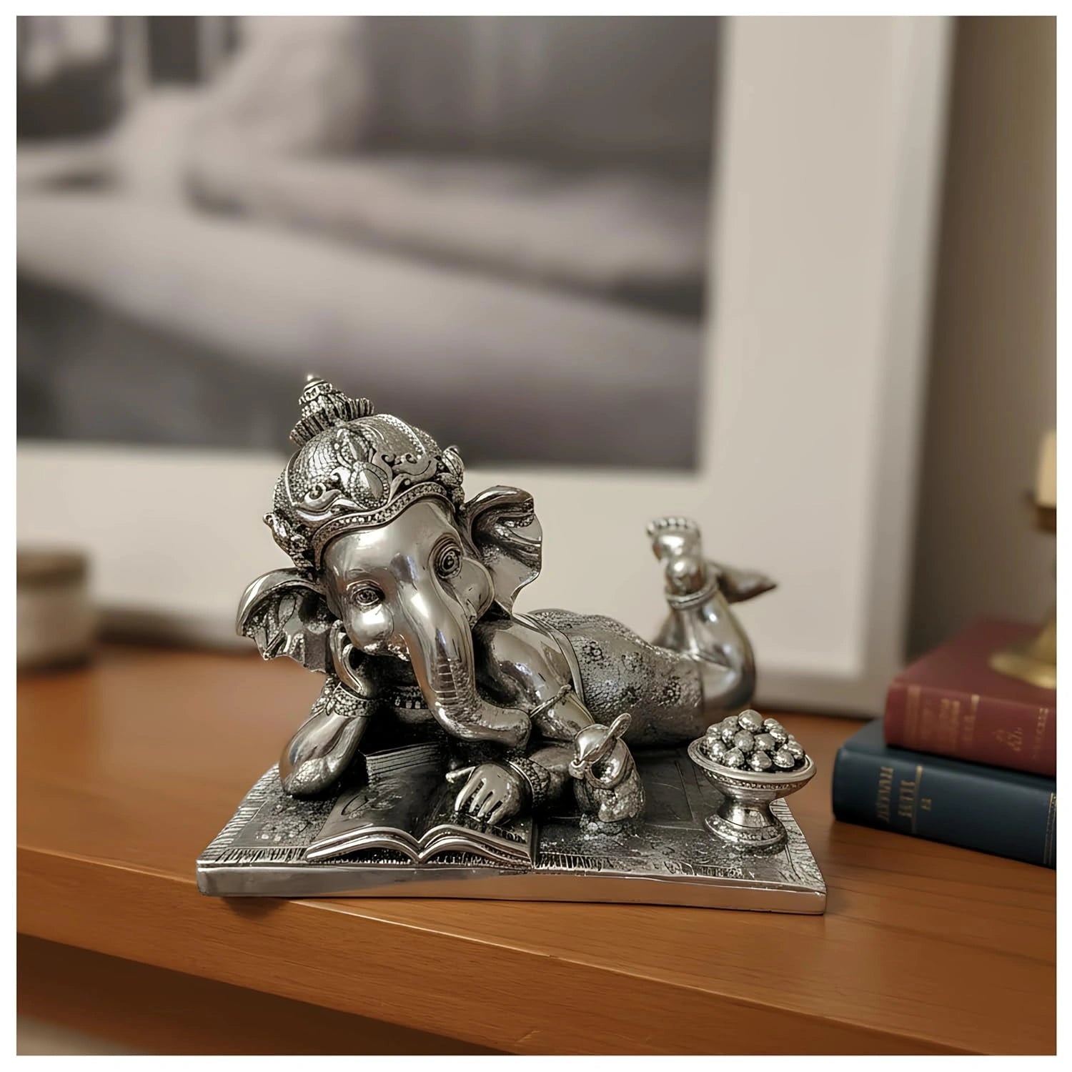 Silver Ganesha idol lying with an open book and a bowl of sweets on a wooden surface