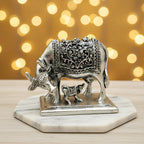 Silver cow and calf figurine with intricate floral engravings on marble base and bokeh background