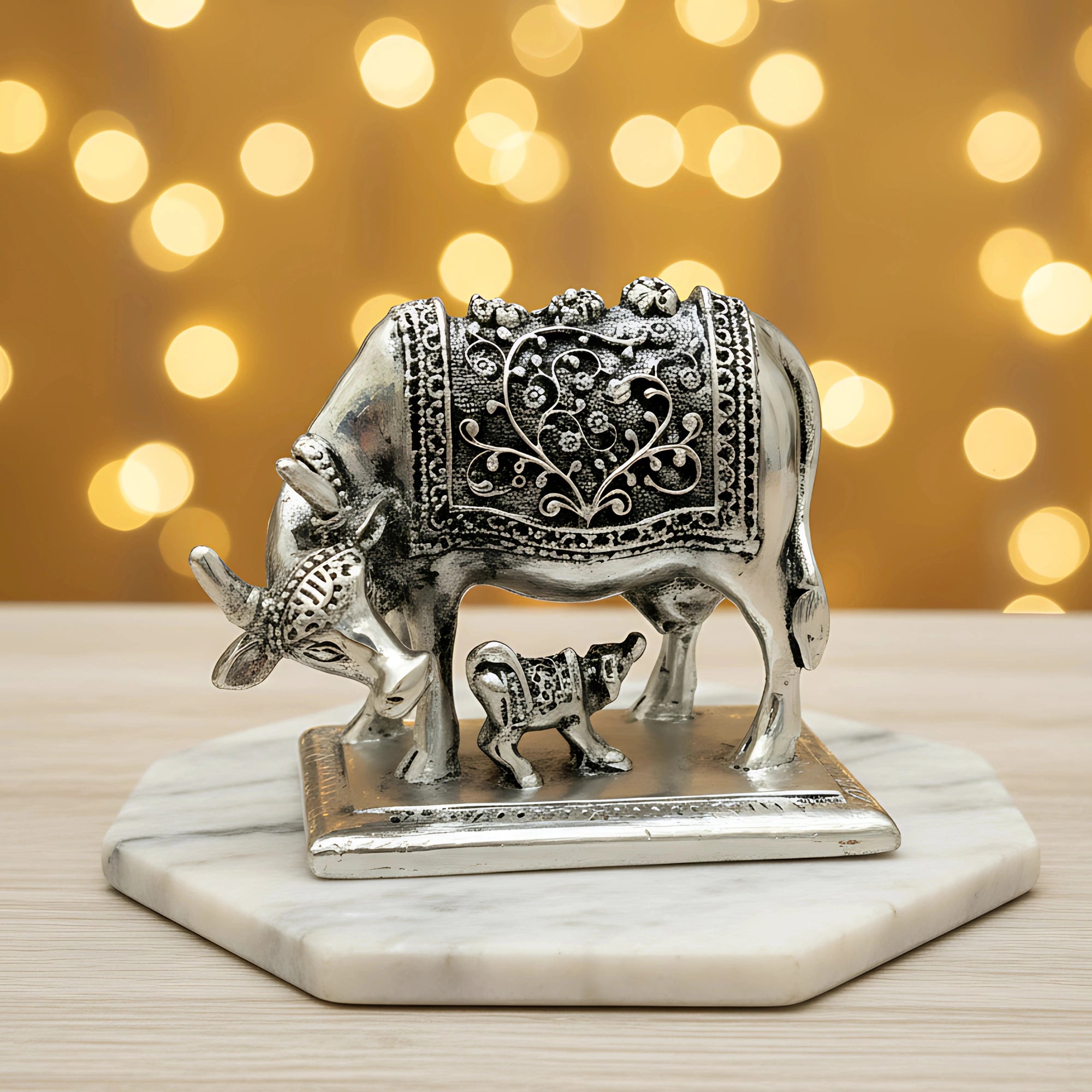 Silver cow and calf figurine with intricate floral engravings on marble base and bokeh background