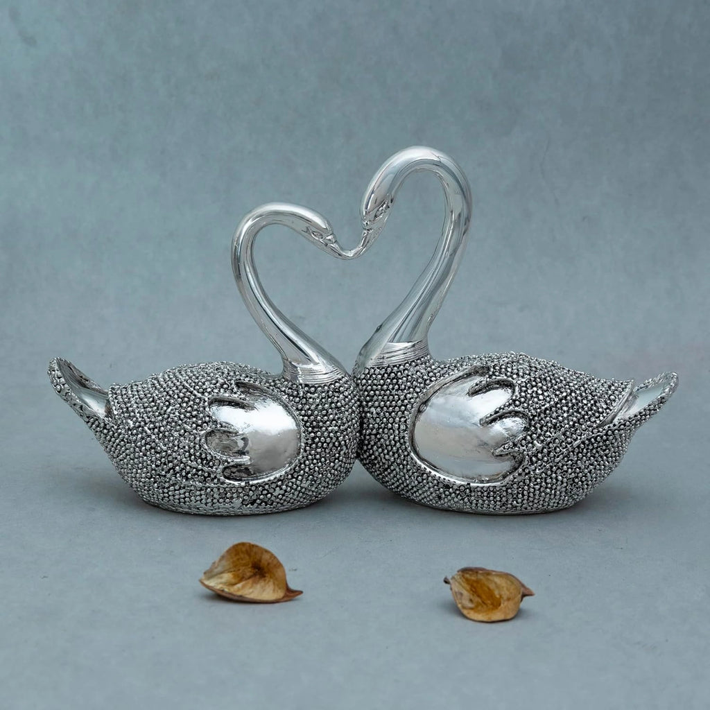 Silver decorative lovebird sculpture with textured bodies and entwined necks forming a heart shape on grey background