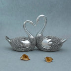 Silver decorative lovebird sculpture with textured bodies and entwined necks forming a heart shape on grey background