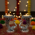 Decorative silver peacock candle holders with lit candles, placed on a colorful festive cloth with bokeh lights