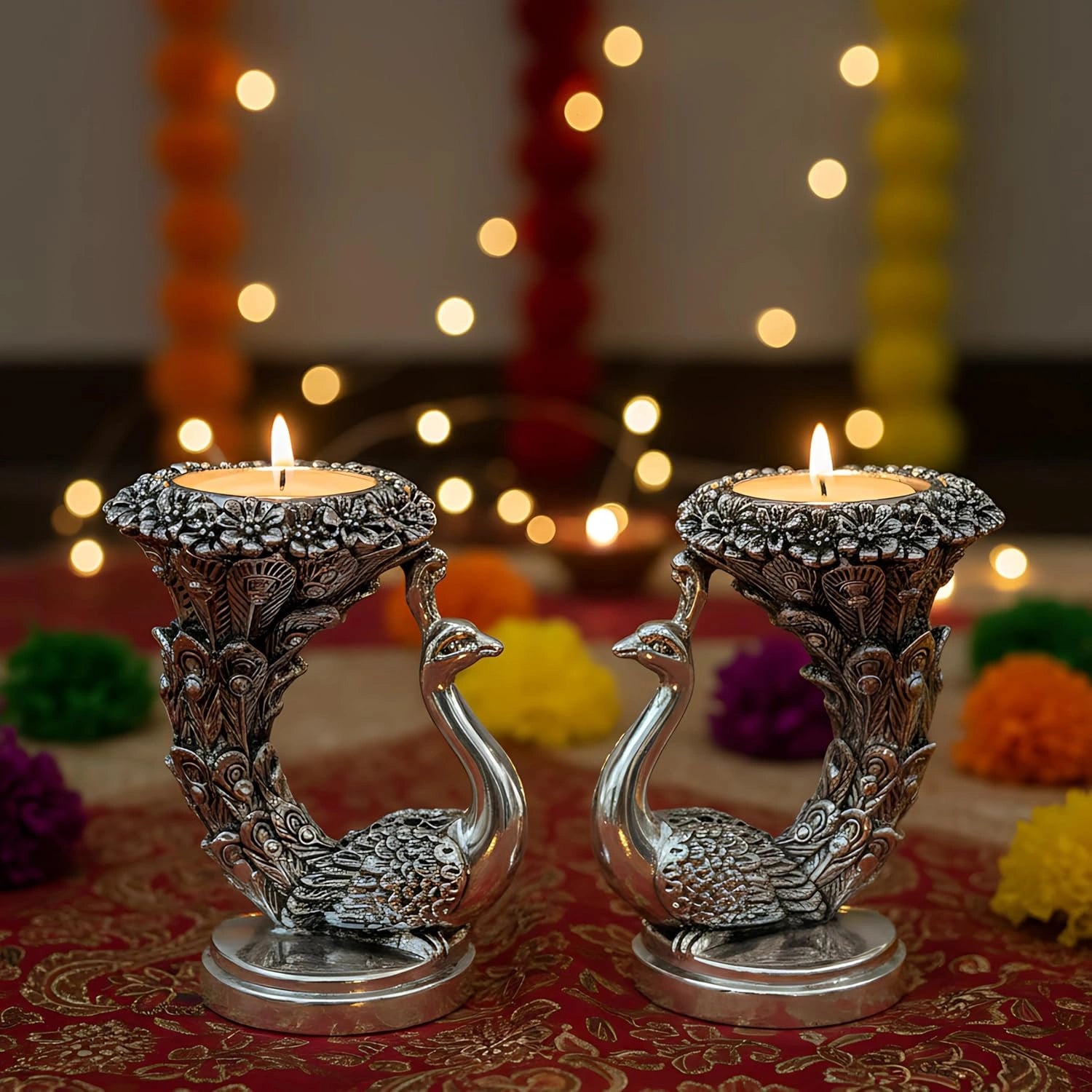 Decorative silver peacock candle holders with lit candles, placed on a colorful festive cloth with bokeh lights