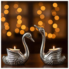 Elegant silver swan-shaped candle holders with lit tealight candles and warm bokeh lights