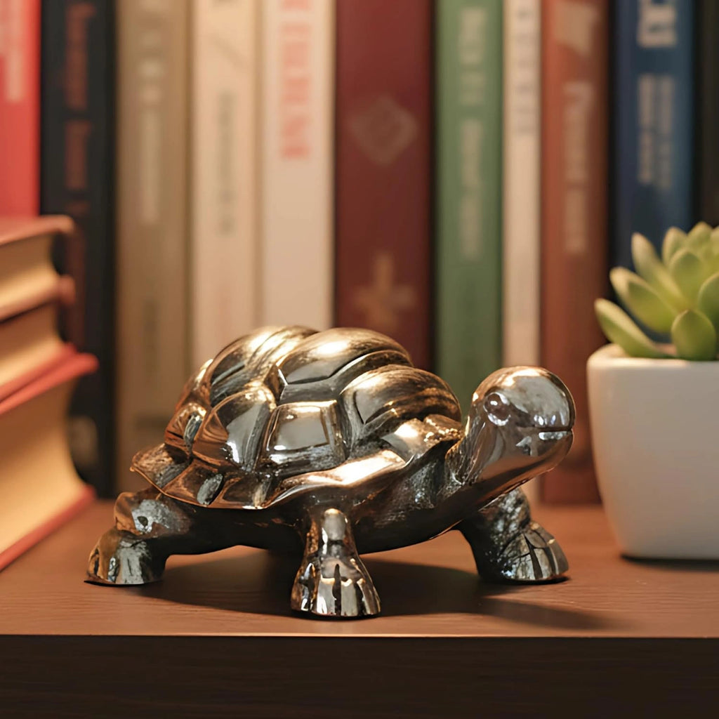 Shiny metallic turtle figurine on wooden shelf with books and a potted succulent