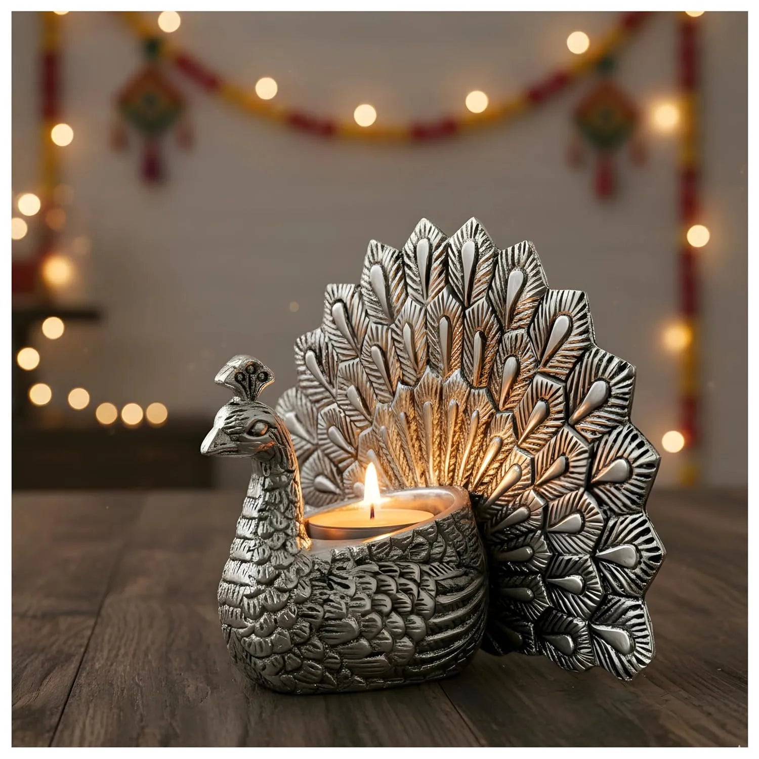 Silver peacock tealight candle holder with lit candle on wooden surface and festive bokeh lights Main image