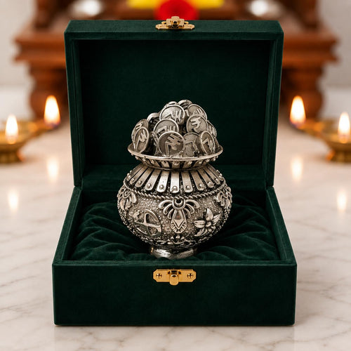 Silver plated kalash khazana brimming with rupee coins in green velvet box near lit diyas