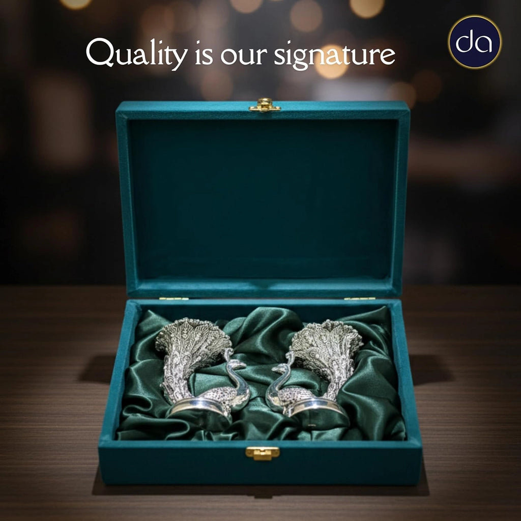 Pair of detailed silver peacock statues displayed in green velvet-lined presentation box on wooden table
