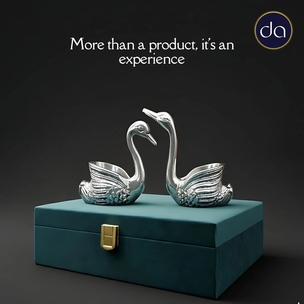 Two polished silver swan figurines on a teal decorative box with gold clasp against dark background