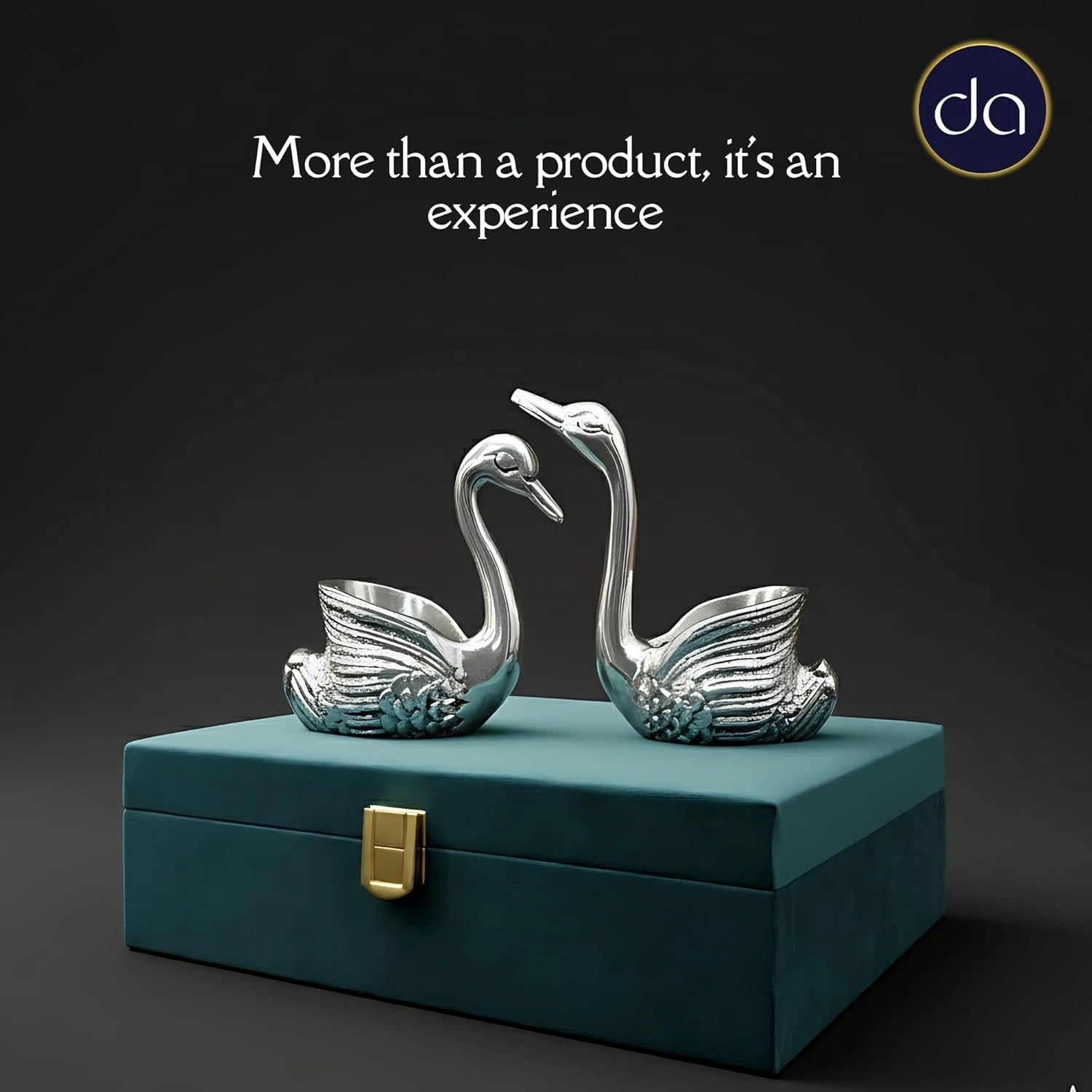Two polished silver swan figurines on a teal decorative box with gold clasp against dark background
