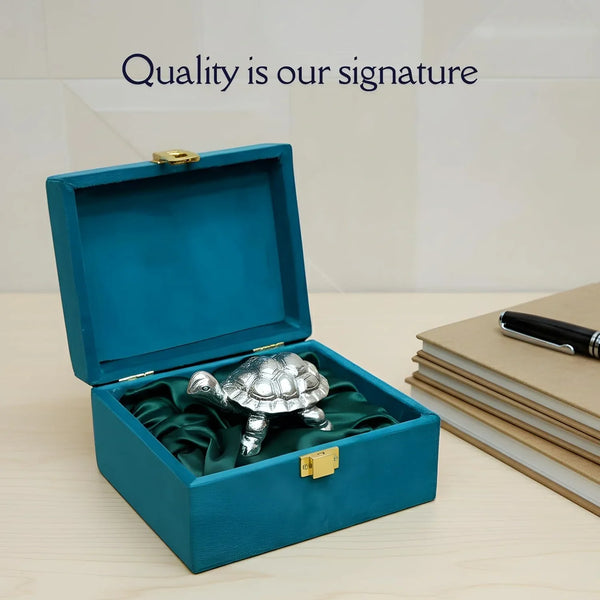 Silver tortoise figurine displayed in an open teal box with green satin lining, next to notebooks and pen