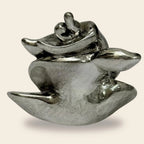Polished silver abstract sculpture with smooth, curving forms on beige background