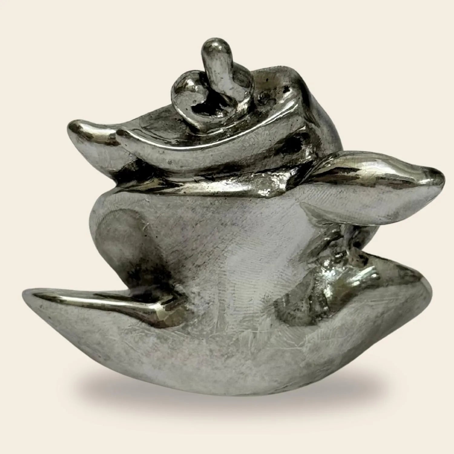 Polished silver abstract sculpture with smooth, curving forms on beige background