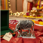 Decorative silver cow statue with calf on red fabric, Indian festive setting with lights and flowers