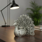 Decorative silver peacock figurine candle holder on wooden table with desk lamp and plant