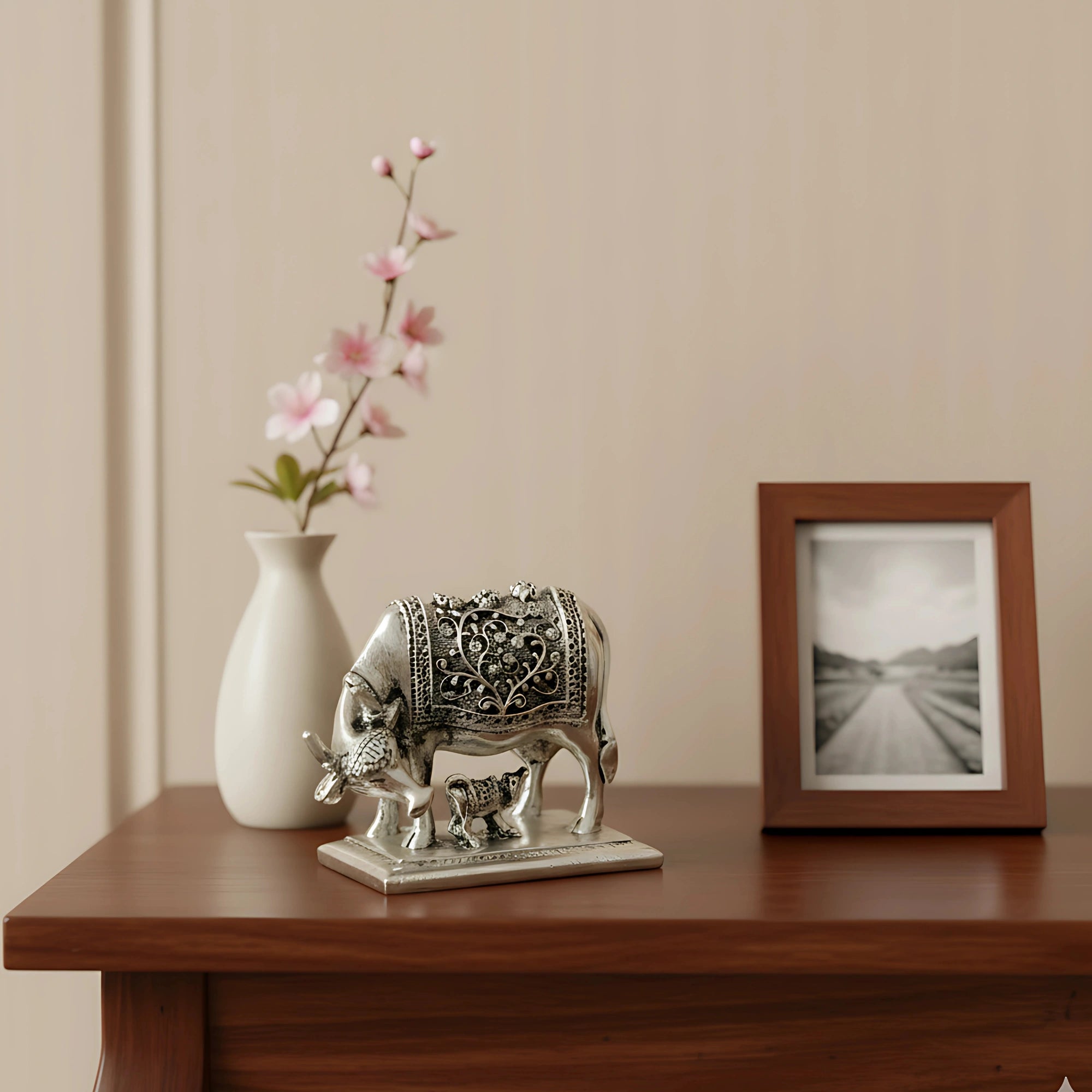 Decorative silver cow and calf statue on wooden table with white vase and photo frame
