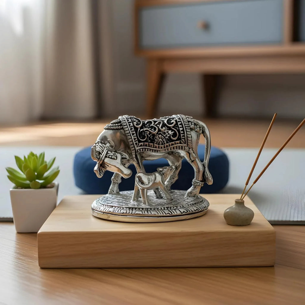 Intricate silver cow and calf sculpture on wooden base with green succulent and incense sticks