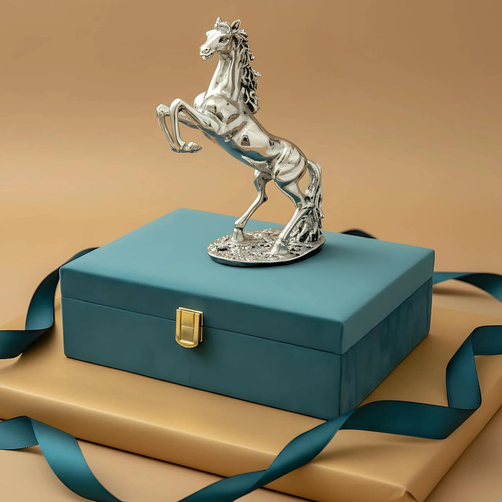 Silver horse statue on teal gift box with gold clasp and ribbon on beige background