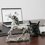 Silver running horse statue on wooden desk with laptop, pen holder, and office supplies
