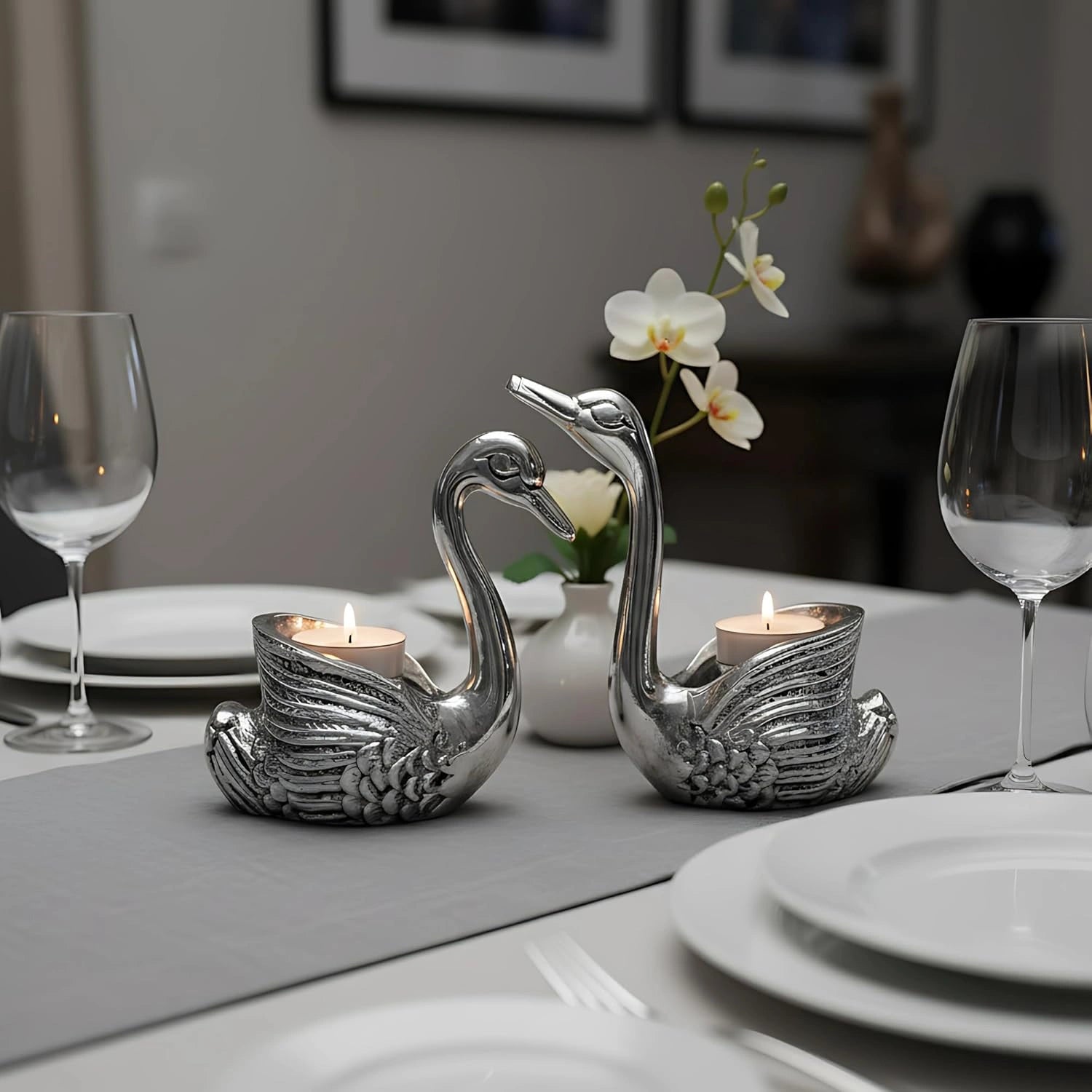 Silver swan-shaped candle holders with lit candles on a modern dining table with glassware and white plates