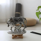 Metal decorative statue of cow and calf with intricate designs on round stand in minimalist room