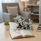 Silver Ganesha idol figurine in reclining pose on a book with sweets, on a wooden table with open book and succulent