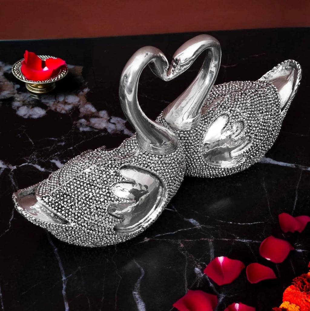 Decorative silver swan couple figurine with necks forming a heart on black marble with rose petals