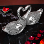 Decorative silver swan couple figurine with necks forming a heart on black marble with rose petals