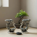 Pair of silver peacock candle holders with intricate feather details on a wooden surface and bonsai plant background