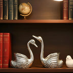 Silver swan pair showpiece on wooden shelf with books, globe, and white bird figurine