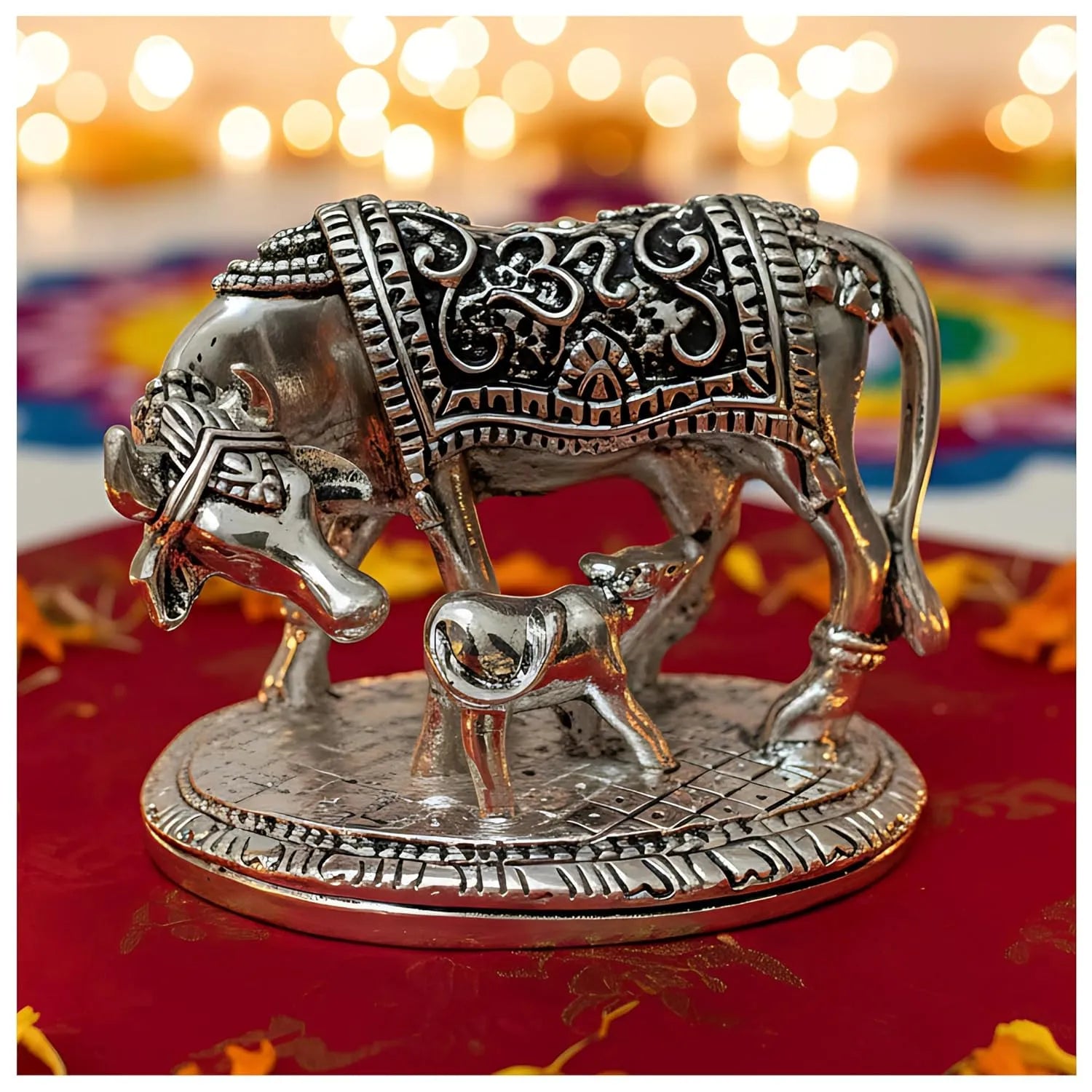 Silver cow statue with calf engraved with intricate traditional patterns on a decorative base