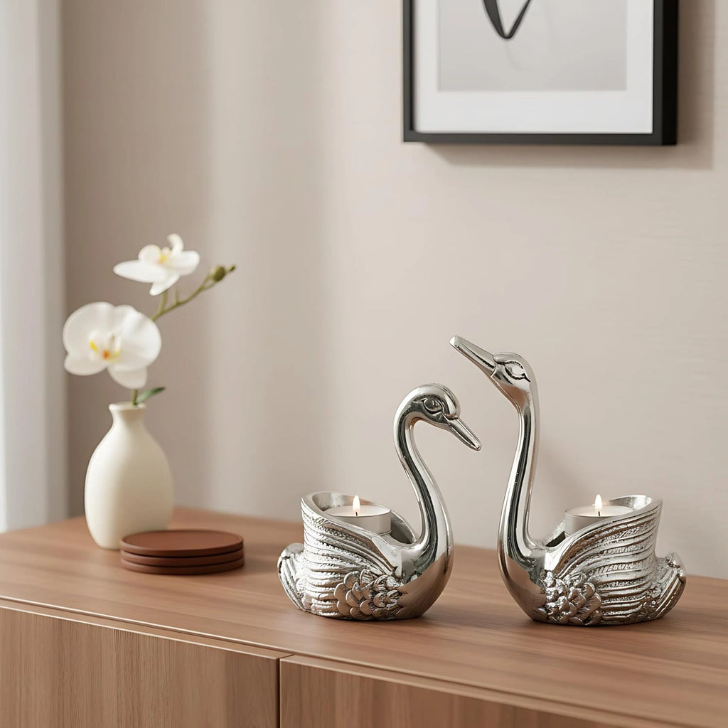 Silver swan candle holders with lit candles on wooden surface next to white orchid in vase