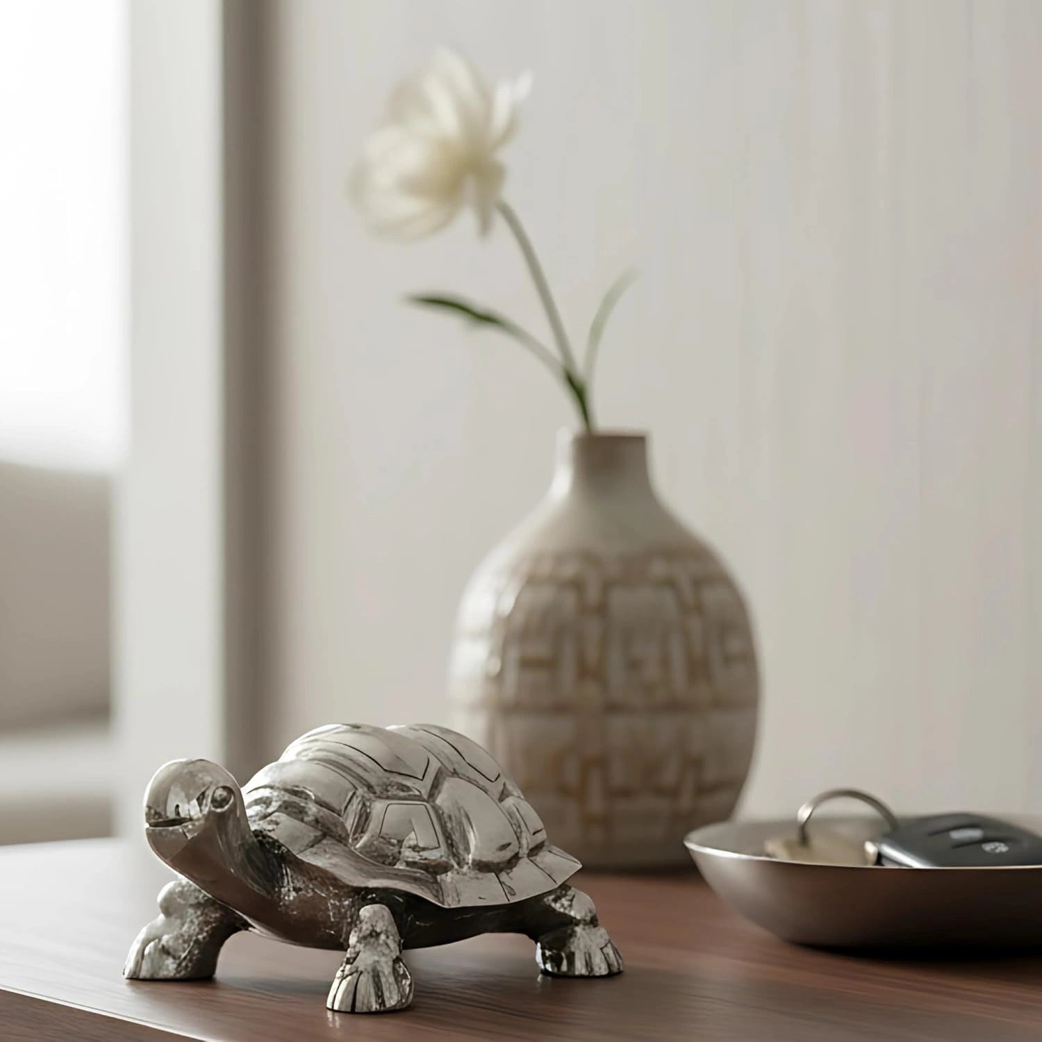 Decorative silver turtle figurine on wooden table with ceramic vase and white flower in background