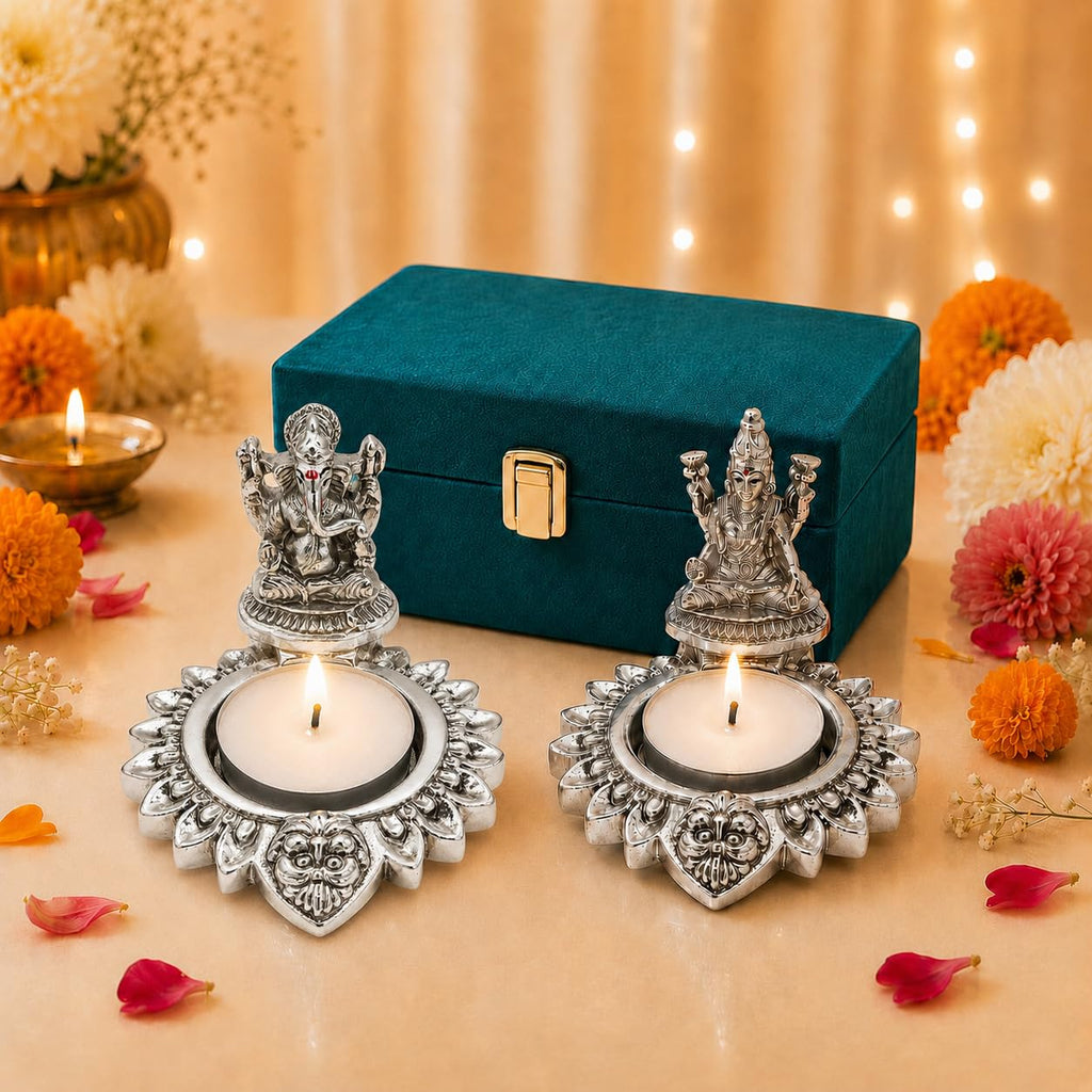 Silver-plated Lakshmi and Ganesha diya pair with lit tealights beside a teal velvet gift box