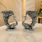 Pair of silver peacock-shaped decorative vases with intricate feather and floral designs on marble surface