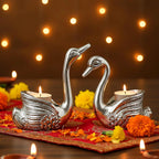 Silver swan-shaped tealight candle holders on red cloth with marigold flowers and warm bokeh lights