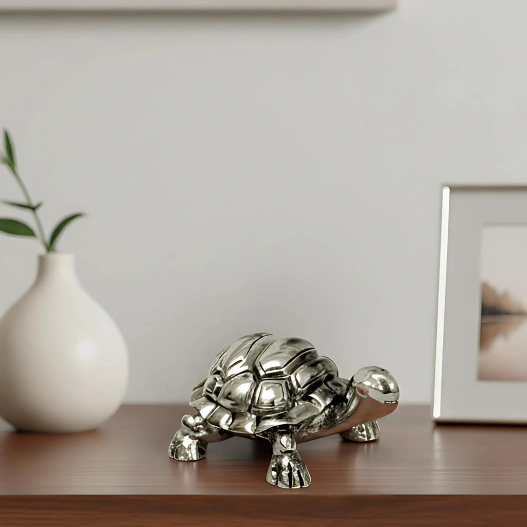 Shiny silver tortoise figurine on wooden surface with white vase and framed wall art background