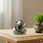 Silver Ganesh idol placed on woven mat on wooden table with bonsai plant and stones