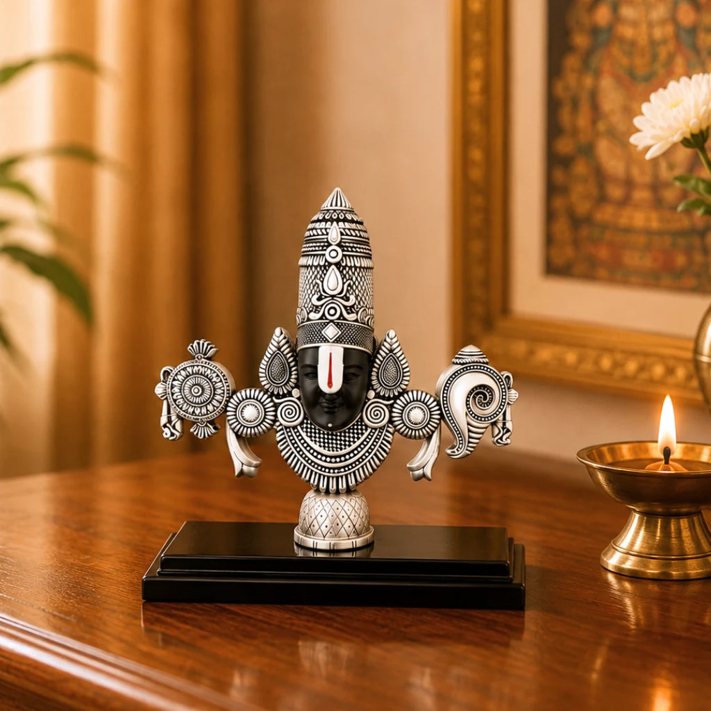 The 8 inch silver Balaji idol on a polished wooden table beside a lit brass diya and a framed painting #silver-8-inch
