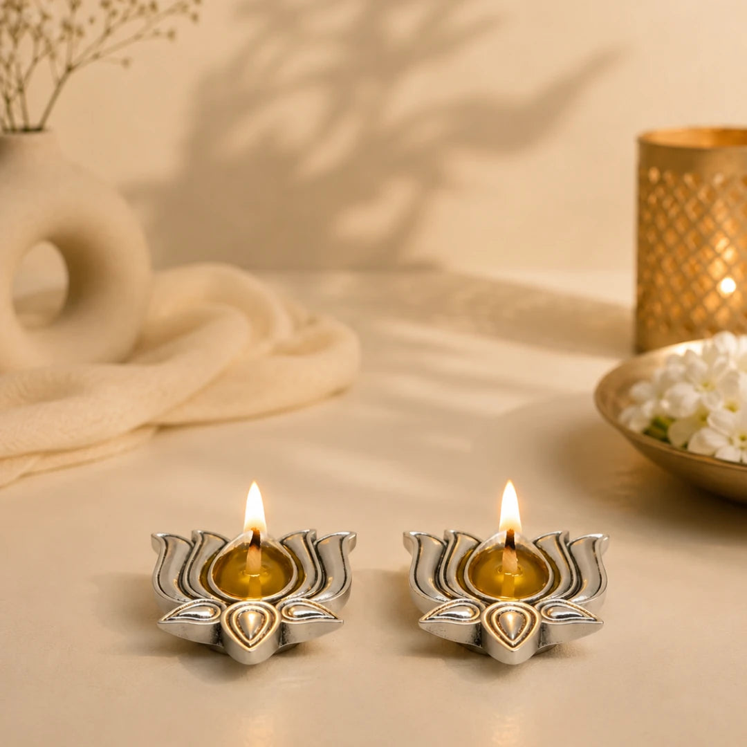 Two lit silver-plated lotus diyas on a beige table with a gold lantern and white flowers #2