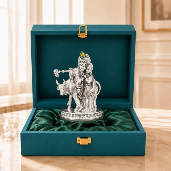 Radha Krishna with cow silver-plated idol resting on green satin inside an open teal velvet gift box